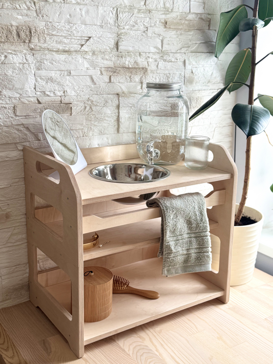 Montessori wooden wash station for kids with stainless steel bowl, water jar, towel rack, and open shelves, handmade from birch plywood.