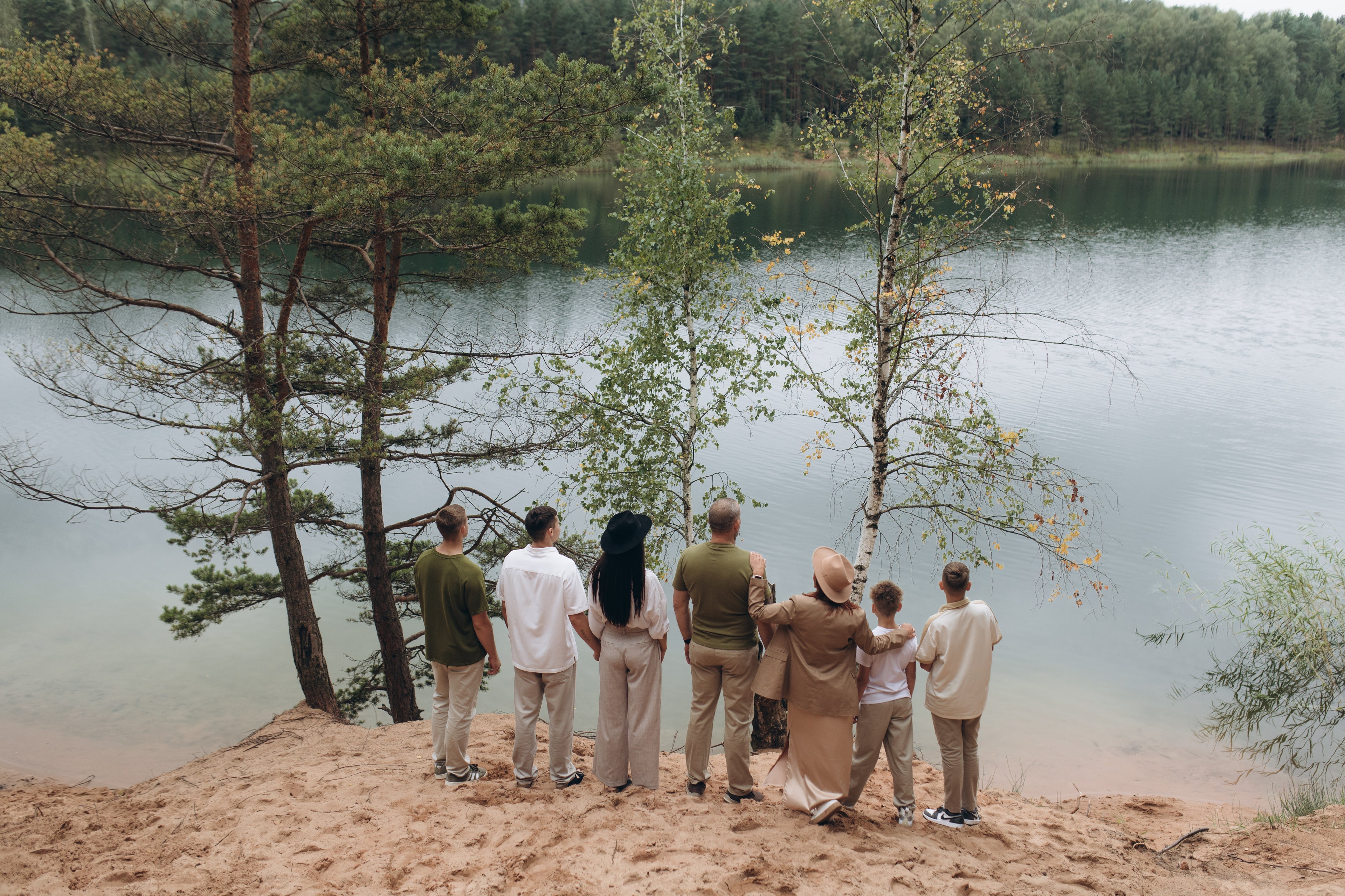 Group of people standing on a sandy shore by a lake with trees in the background